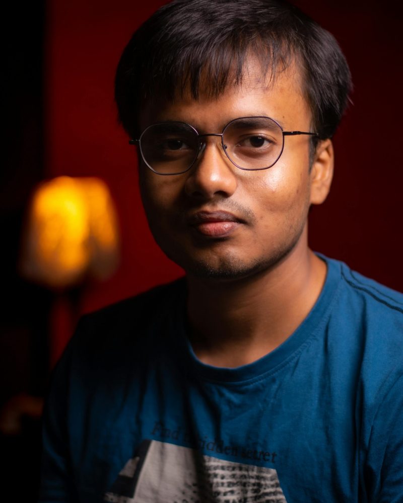 Casual portrait of a young man with glasses, captured indoors with warm lighting.